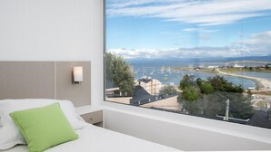 Habitación de hotel con un ventanal grande que ofrece vistas a un puerto deportivo y la zona costera.