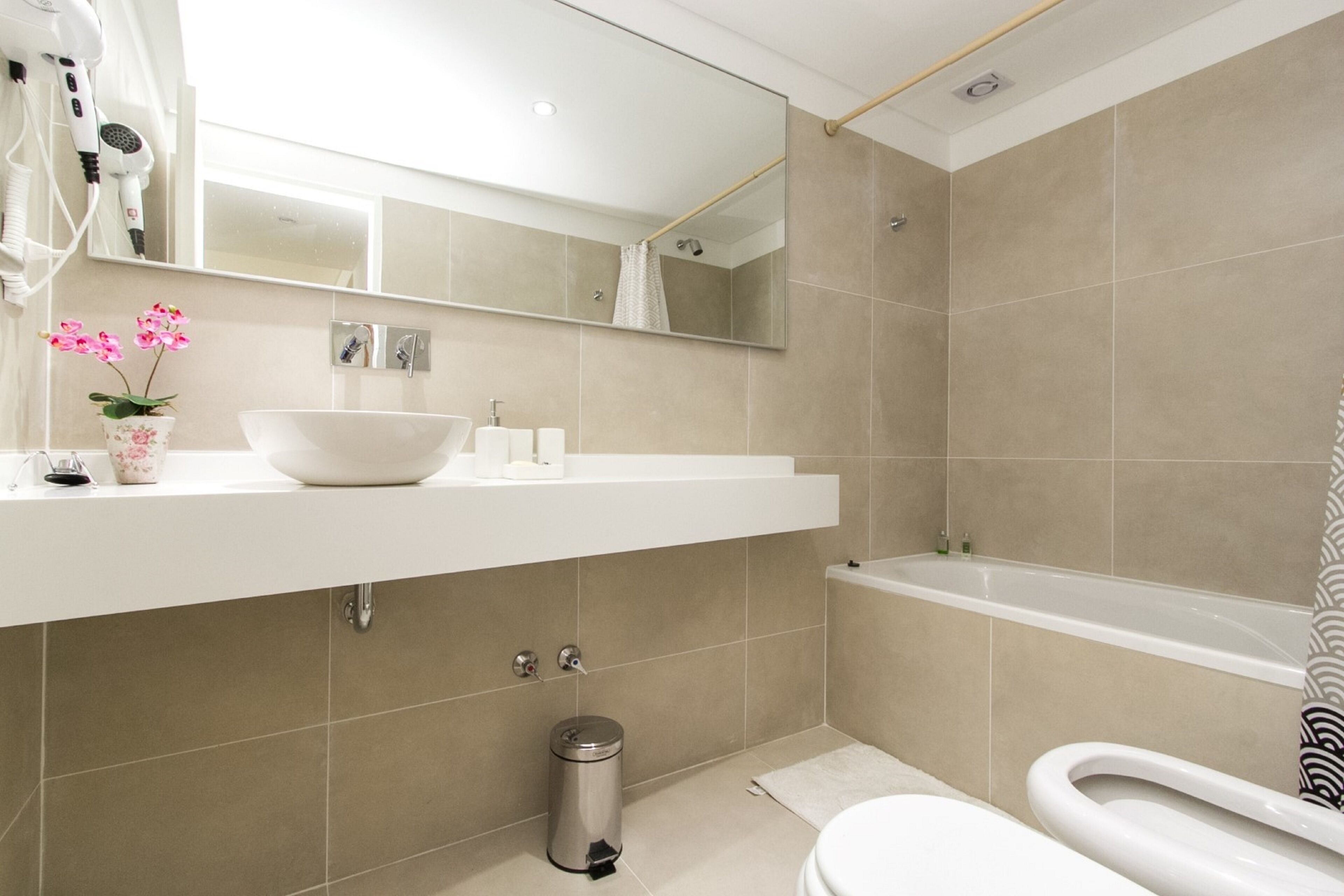 A modern bathroom with a white sink, a large mirror, a bathtub, and a toilet.