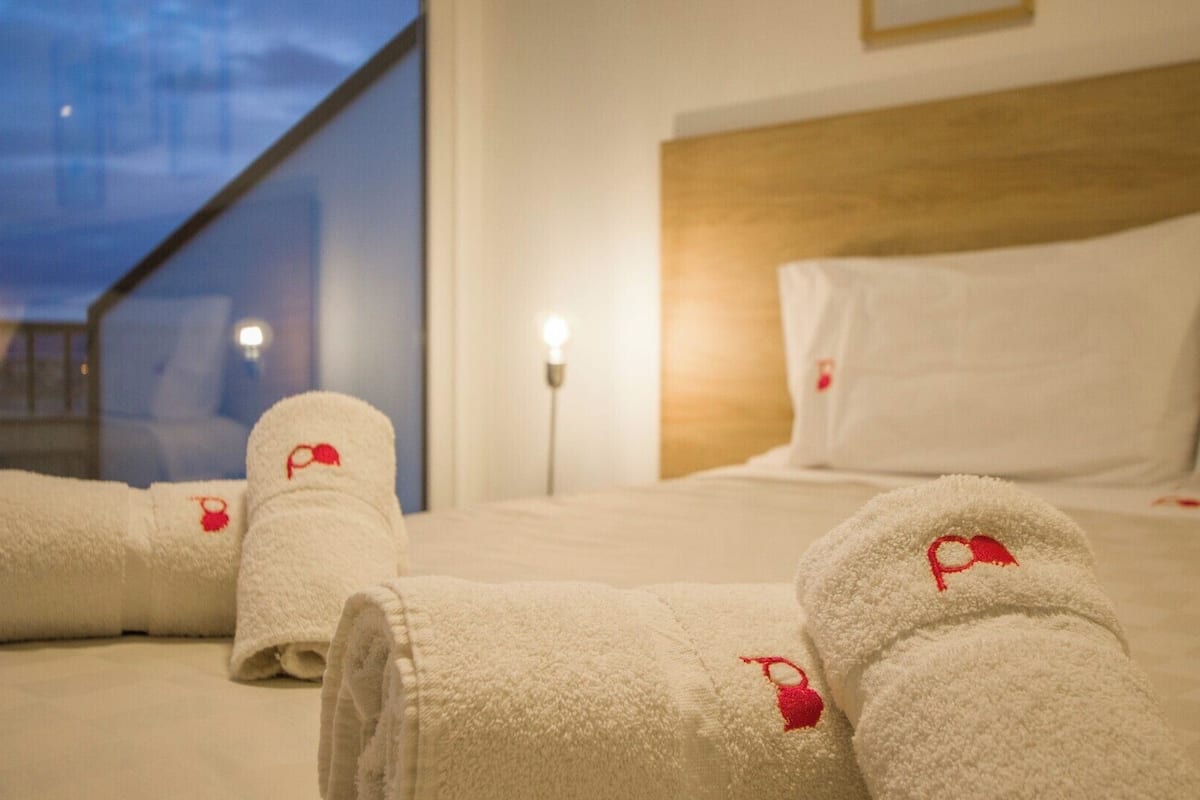 Habitació d'hotel amb un llit, almoines i tovalloles enrotllades amb un logotip vermell.