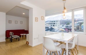 Ein modernes Wohnzimmer mit einem roten Sofa, einem Esstisch mit Stühlen und einem großen Fenster mit Blick auf die Stadt.