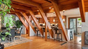 A spacious loft-style room with exposed wooden beams, a dining area with a table and chairs, and a kitchen area with bar stools. - The Great Escape - Picturesque Sebago Lake (Raymond)