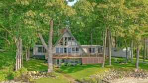 A two-story house with a balcony, surrounded by trees and a well-maintained lawn. - The Great Escape - Picturesque Sebago Lake (Raymond)