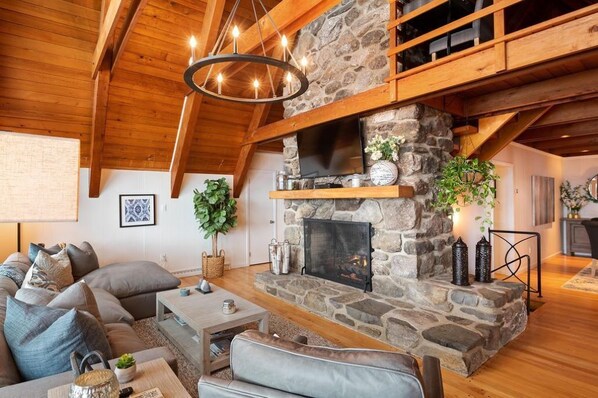 A cozy living room with a stone fireplace, wooden beams, and a comfortable seating area. - The Great Escape - Picturesque Sebago Lake (Raymond)