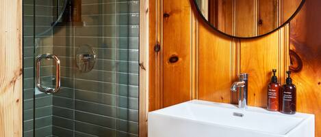A bathroom with a glass-enclosed shower, a white sink, and wooden paneling.