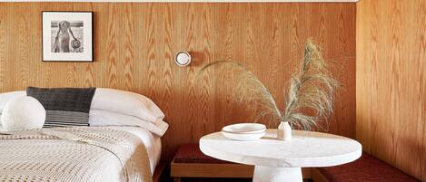 A bedroom with a bed, bedside table, and a small seating area with a table and bench.
