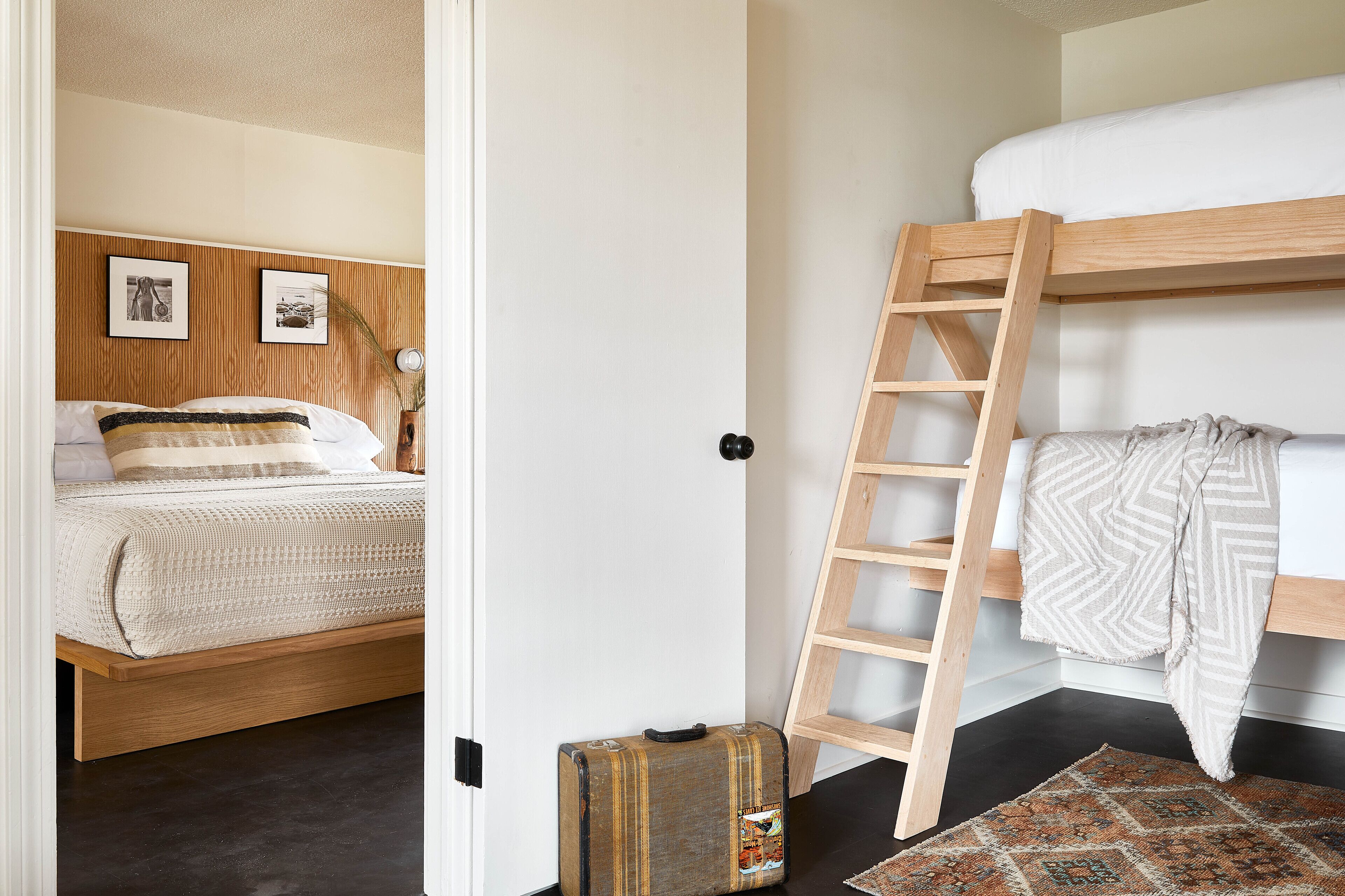 A bedroom with a bunk bed, a wooden ladder, a suitcase, and a patterned rug.