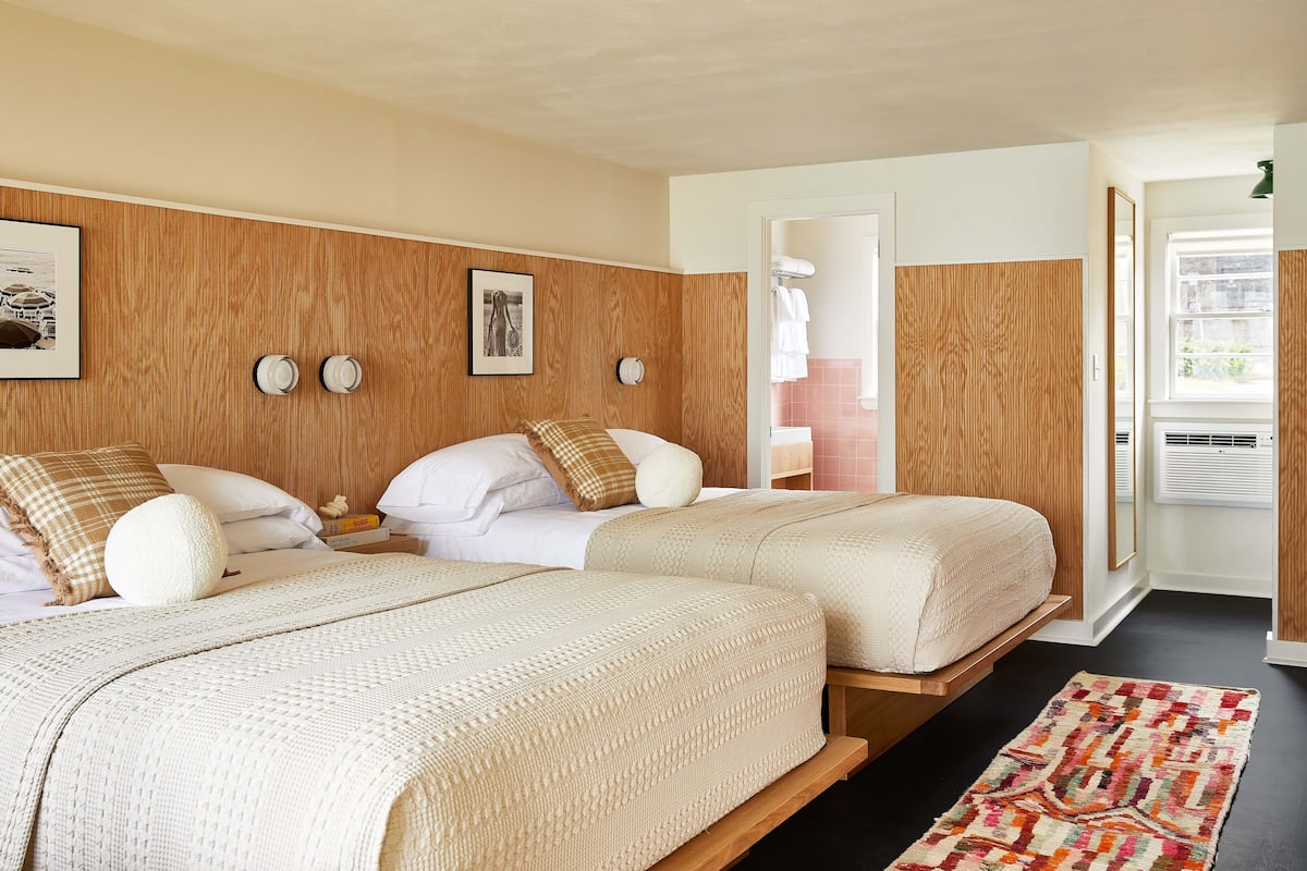 Ein Schlafzimmer mit zwei Betten, Holzvertäfelung an den Wänden, einem gemusterten Teppich und einem gerahmten Bild.