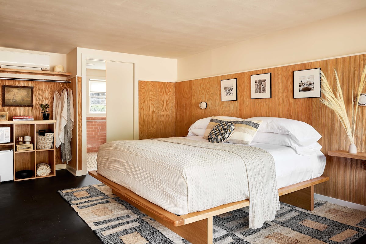 Ein Schlafzimmer mit einem Holz-Kopfteil, einem Bett mit weißer Bettwäsche, einem Nachttisch und einem an der Wand befestigten Regal.