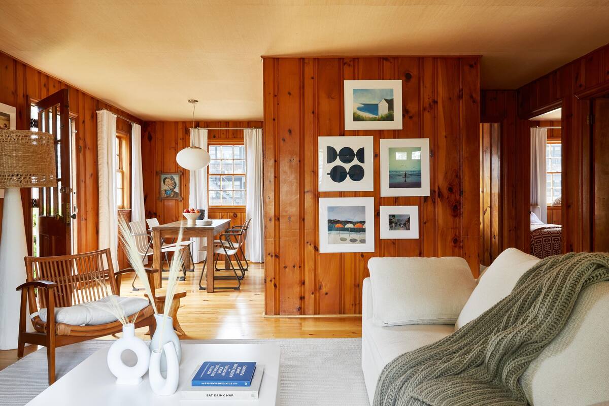 Ein Zimmer mit Holzwänden, einem Essbereich, einem weißen Sofa und einem Tisch mit Büchern und Vasen.