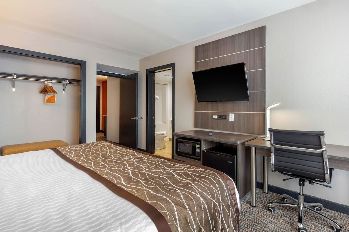 Een hotelkamer met een groot bed, een bureau met een flatscreen-tv, een magnetron en een stoel.