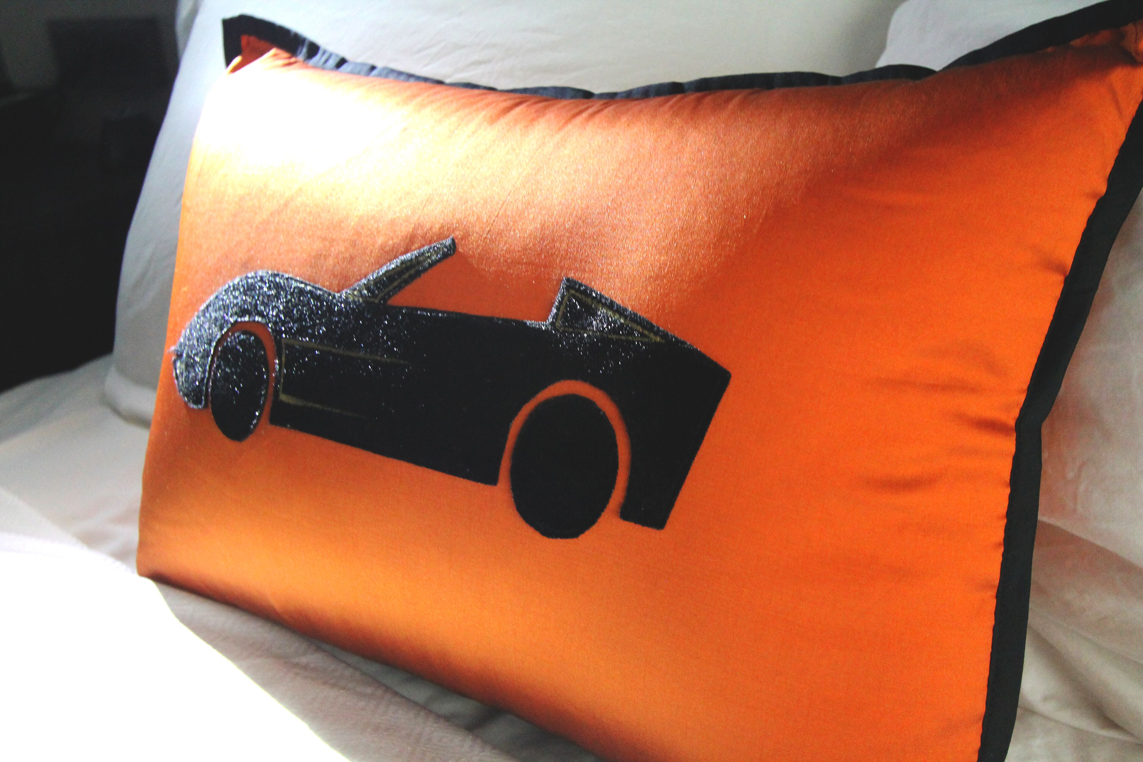 A pillow with a black car design on an orange background.
