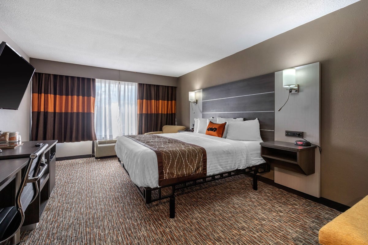 Een hotelkamer met een bed, nachtkastje, lamp en een bureau met stoel.