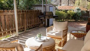 Een terras met rieten meubels, een barbecue en een kleine schuur.