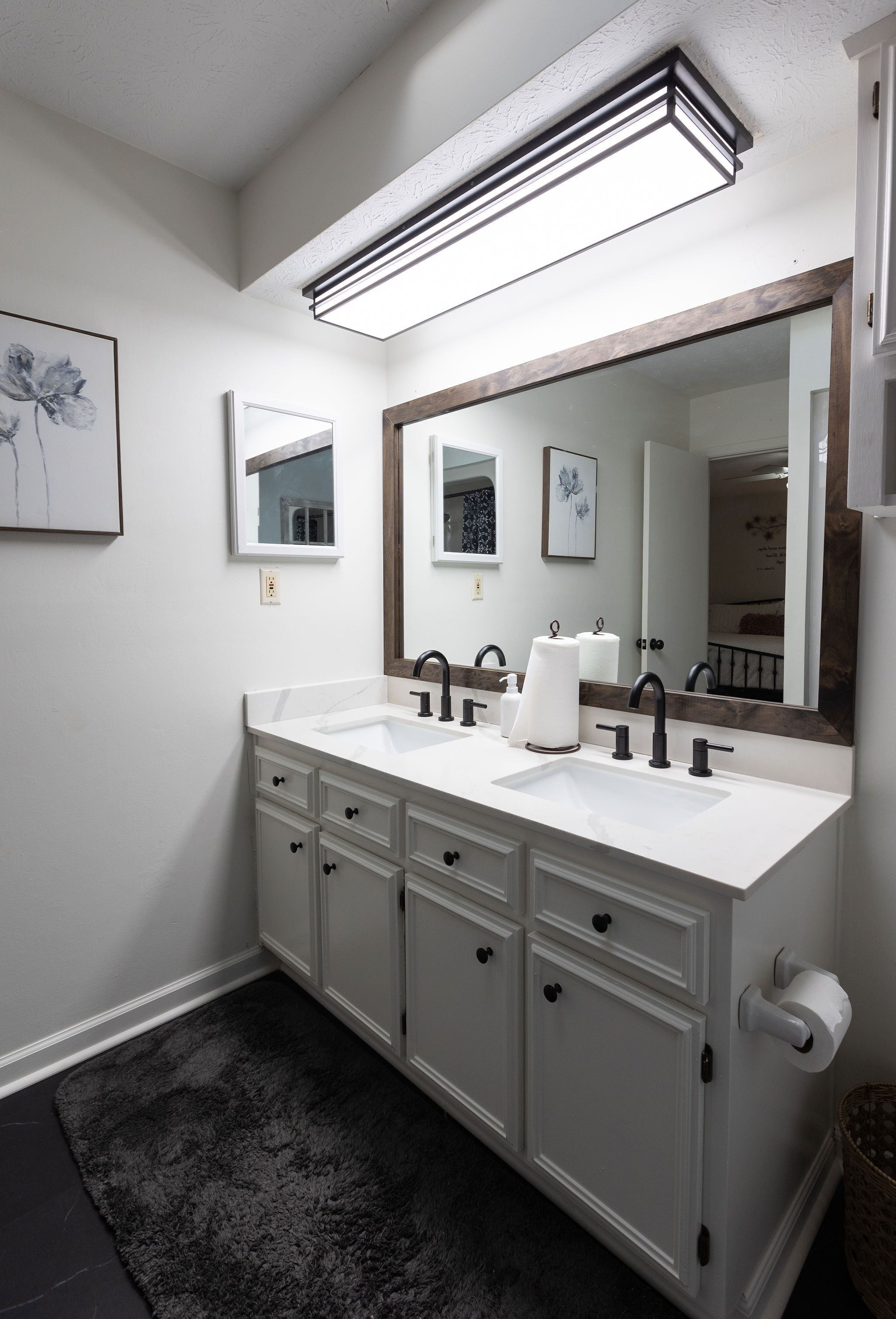 A modern bathroom with two sinks, a large mirror, and a dark rug.