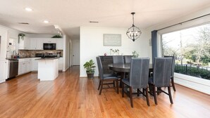 Een moderne keuken met witte kasten, een centraal eiland en een eethoek met een donker houten tafel en stoelen.