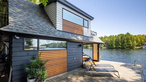 Ein modernes Haus mit einem Steg, der über einen See führt, mit einem großen Fenster und einer Holzterrasse.