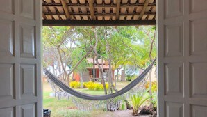 An open door with a view of a hammock, trees, and a building in the background. - Pousada Vila Rosa (Porto Seguro)