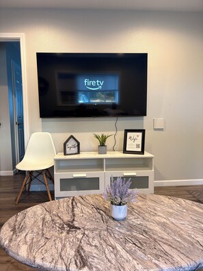 A living room with a flat-screen TV mounted on the wall, a white chair, a round marble coffee table, and a small potted plant. - Keizer Valley Estate I 3BR Family Stay Near Salem Oregon (Keizer)