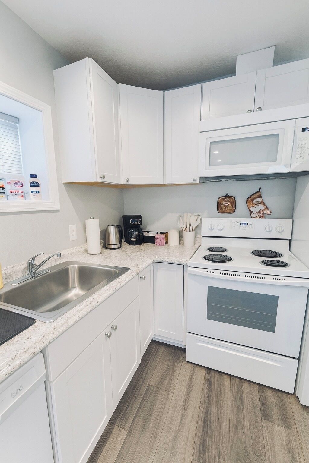 A kitchen with white cabinets, a stainless steel sink, a microwave, a coffee maker, and a stove.