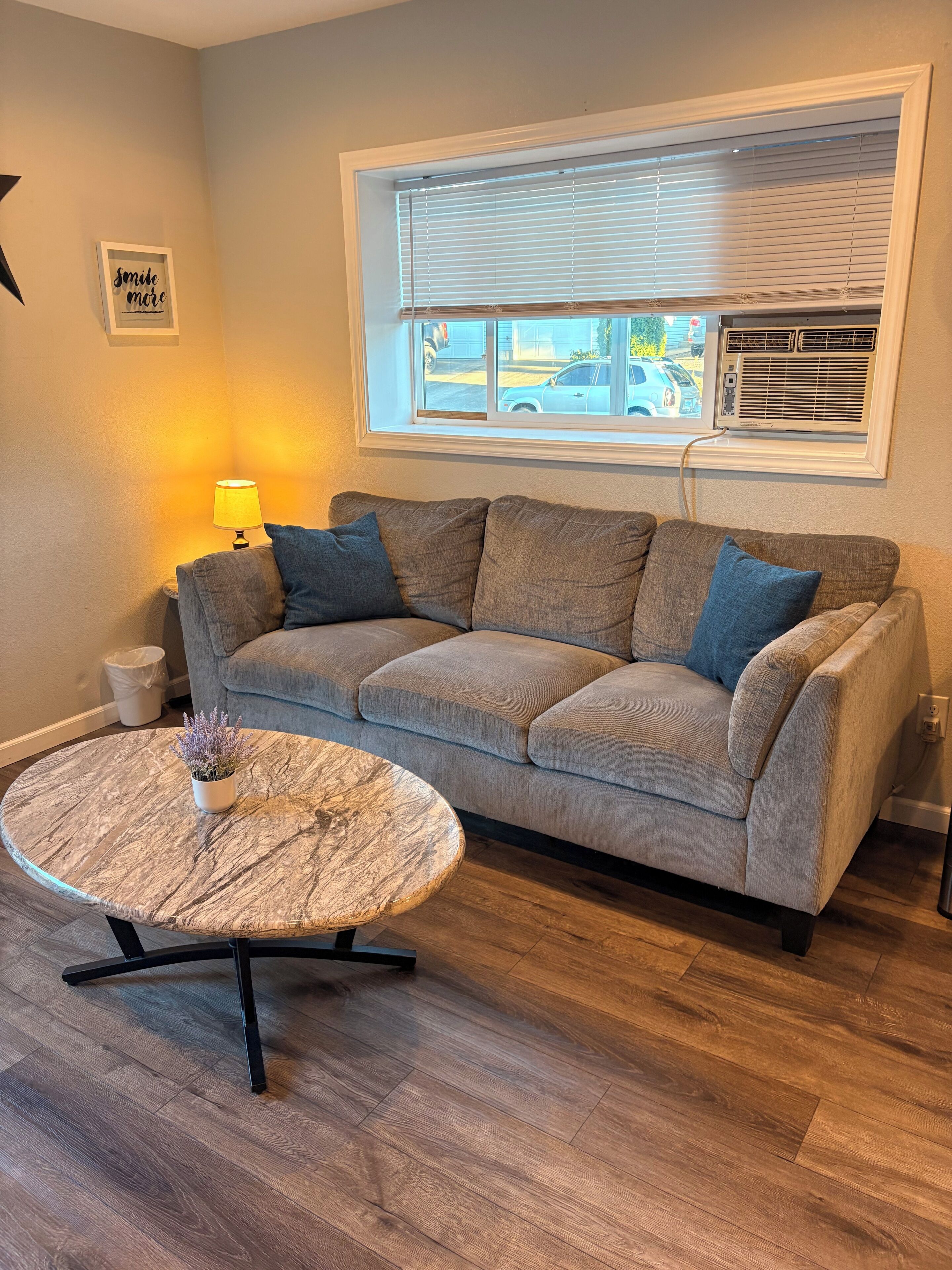 A living room with a sofa, a round coffee table, a lamp, and a window with blinds.