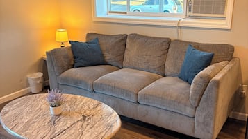A living room with a sofa, a round coffee table, a lamp, and a window with blinds.