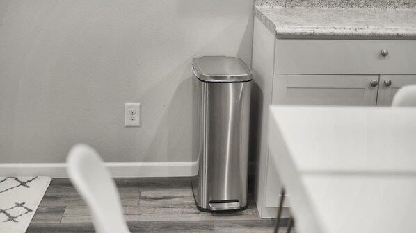 A kitchen with a stainless steel trash can, a white countertop, and a wooden floor. - Keizer Valley Estate I 3BR Family Stay Near Salem Oregon (Keizer)