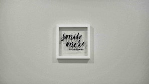 Un letrero en marco con la inscripción 'smile more' sobre una pared lisa.