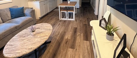 Un espace de vie moderne comprenant un canapé, une table basse, un téléviseur et, au fond, un coin cuisine.