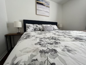 Ein ordentlich gemachtes Bett mit floralem Bettbezug, zwei Nachttischlampen und einem gerahmten Bild an der Wand.