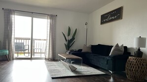 A living room with a dark blue sofa, a coffee table, a lamp, a wicker side table, and a large plant. - Modern Jewel : No Stairs : 3 bedrooms : Sleeps 6 : Pool Open : Views (Branson)