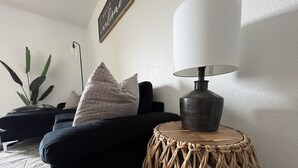 A modern living room with a dark sofa, a round woven side table, and a lamp. - Modern Jewel : No Stairs : 3 bedrooms : Sleeps 6 : Pool Open : Views (Branson)