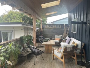 An outdoor lounge area with wooden furniture, a wooden table, and potted plants. - Walk to town and beach with beautiful views (Raglan)
