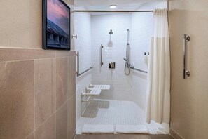 A modern shower area with a glass door, a bench, and a handheld showerhead.