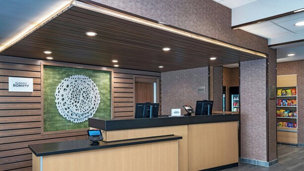 A hotel reception area with a wooden reception desk, a large decorative wall piece, and a sign indicating the hotel name. - Fairfield by Marriott Inn & Suites Phoenix West Chandler (Phoenix)