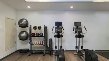 Une salle de sport à domicile équipée de matériel d’exercice, notamment un tapis de course, un vélo elliptique et un support avec divers poids et ballons lestés.