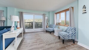A living room with a blue sofa, two patterned chairs, a white console table, and a large window with curtains. - 5611- King's Landing - Nags Head Coastal Condo Near The Beach (Nags Head)