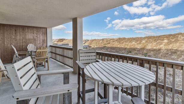 A covered outdoor area with a wooden deck, chairs, and a table. - 5611- King's Landing - Nags Head Coastal Condo Near The Beach (Nags Head)