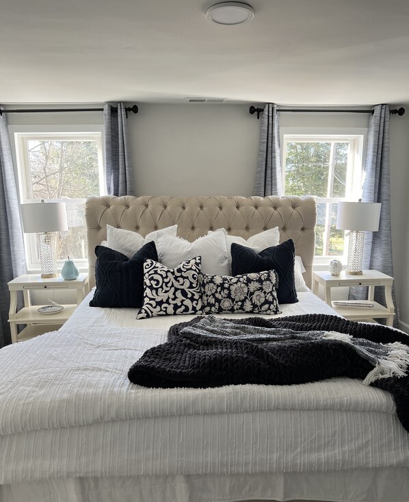 A bedroom with a tufted headboard, multiple pillows, a bedspread, and two bedside tables with lamps.