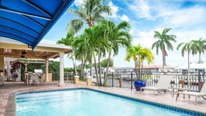 A swimming pool with a blue canopy, surrounded by palm trees and lounge chairs. - Palm Villa: New Remodel / Waterfront / Salt Water Pool! (Pompano Beach)