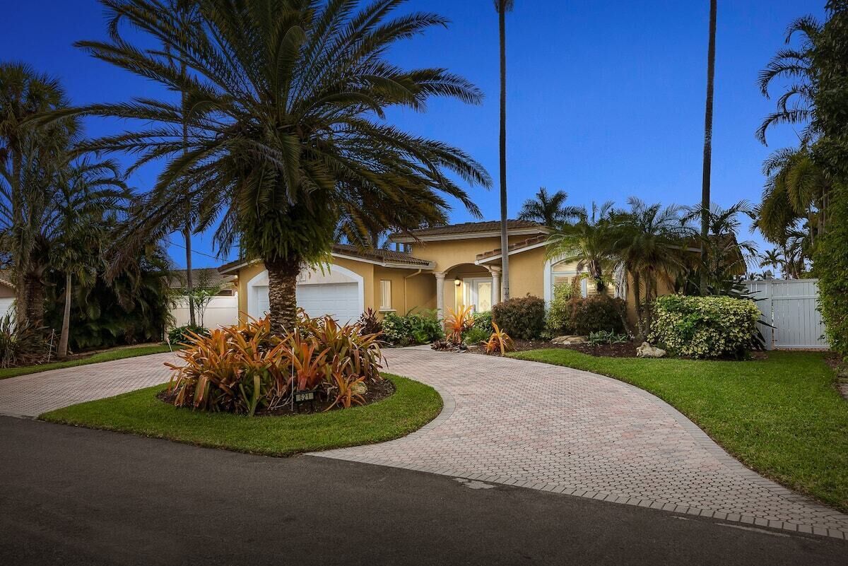 A residential house with a paved driveway, palm trees, and a well-maintained lawn.