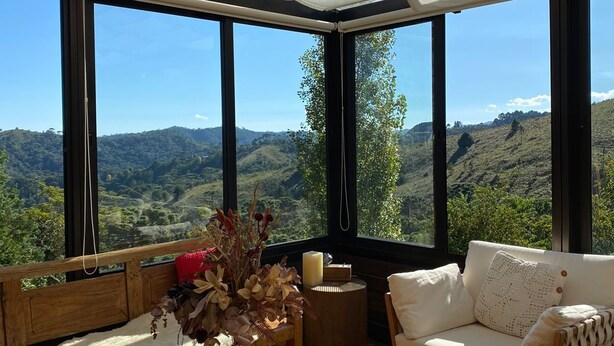Ein gemütlicher Sitzbereich mit Blick auf eine gebirgige Landschaft, ein Holztisch mit Kerzen und ein großes Fenster.