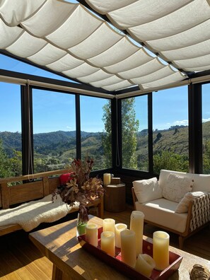 Ein gemütlicher Sitzbereich mit Blick auf eine gebirgige Landschaft, ein Holztisch mit Kerzen und ein großes Fenster.