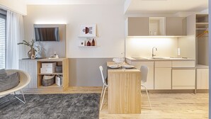 Ein moderner, kompakter Wohnraum mit Essbereich, Küchenzeile und einem an der Wand befestigten Fernseher.