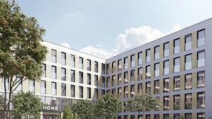 Ein modernes Gebäude mit einem Schild mit der Aufschrift „HOME“, umgeben von angelegten Gärten und Sitzbereichen.