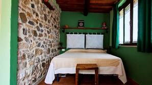 A room with a stone wall, a bed with a white bedspread, a wooden bench, and a window with green curtains. - A cozy nest for a pair (Civitella Paganico)
