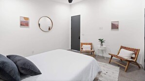 Une chambre moderne avec un lit, deux chaises, un miroir rond et un ventilateur de plafond.