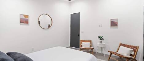 A modern bedroom with a bed, two chairs, a round mirror, and a ceiling fan.
