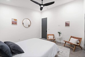 A modern bedroom with a bed, two chairs, a round mirror, and a ceiling fan. - Modern Home w/ Heated Pool (Phoenix)