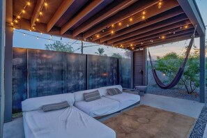 A modern outdoor seating area with a sofa and cushions, a hammock, and string lights. - Modern Home w/ Heated Pool (Phoenix)