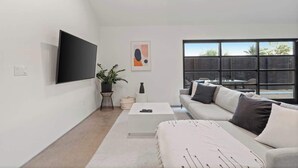 Un salon moderne avec un téléviseur à écran plat, un canapé, une table basse et une grande fenêtre.
